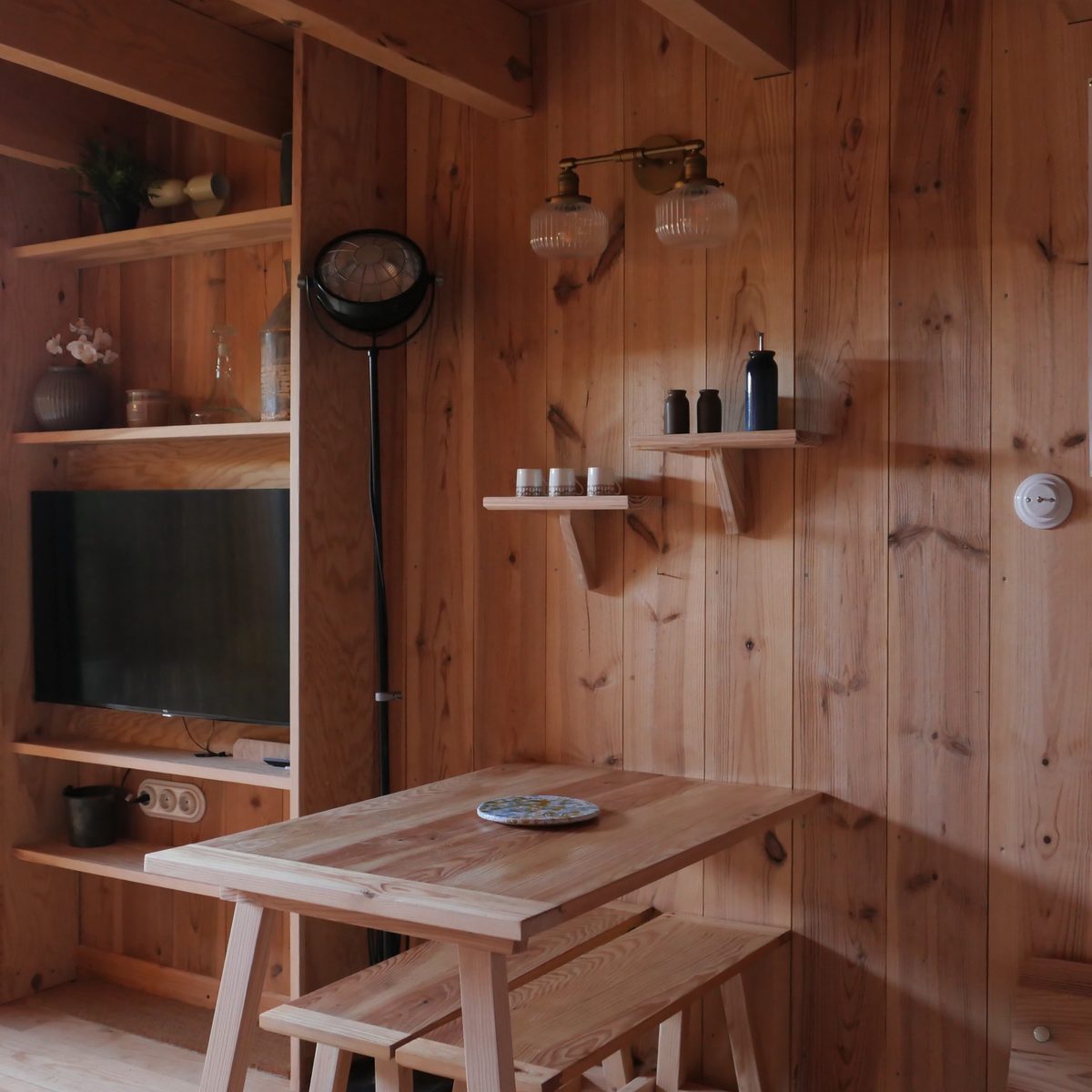 Séjour avec table et bancs en bois, étagères et télévision